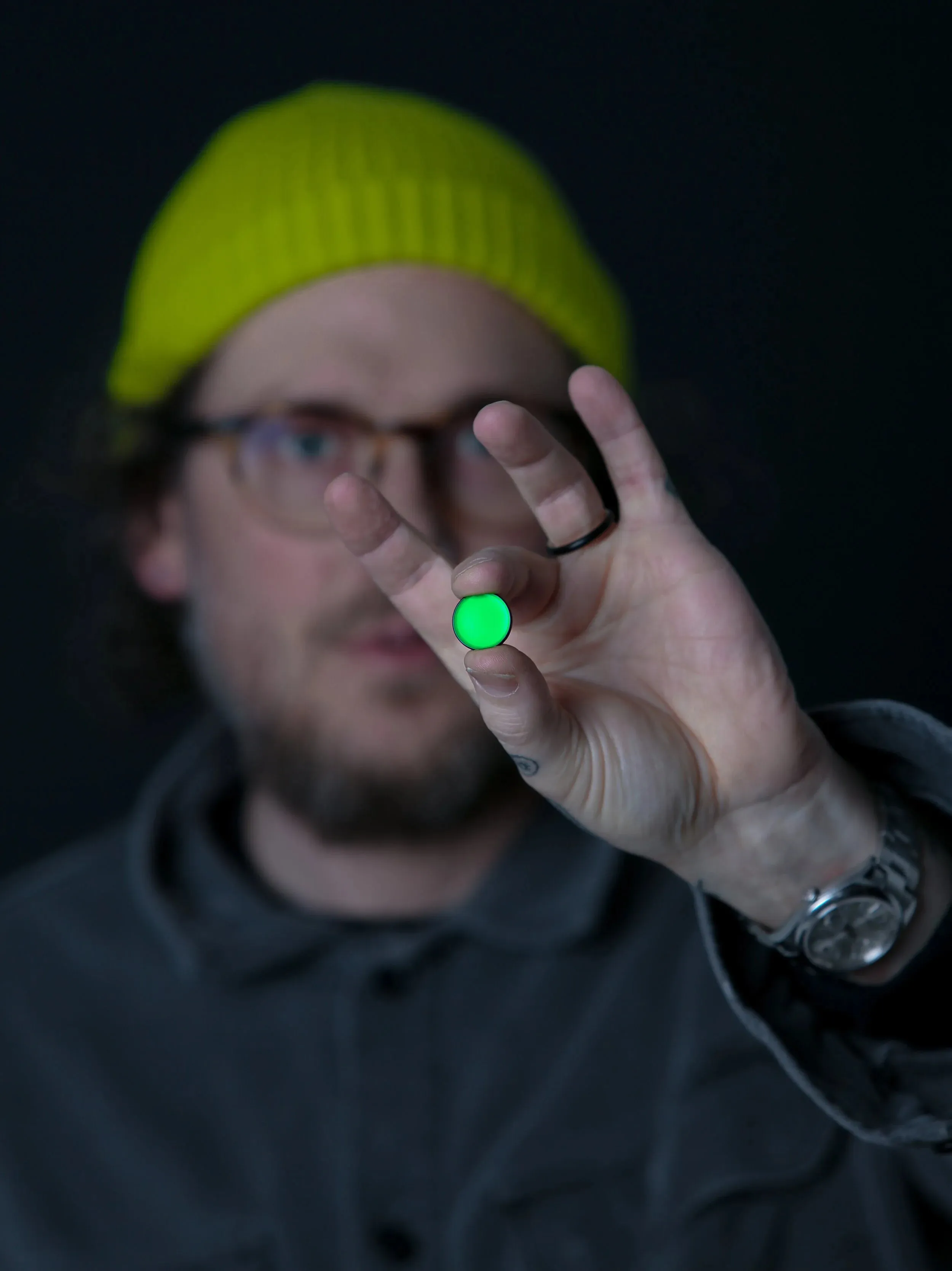 A person holding up a small green enamel Green Dot badge